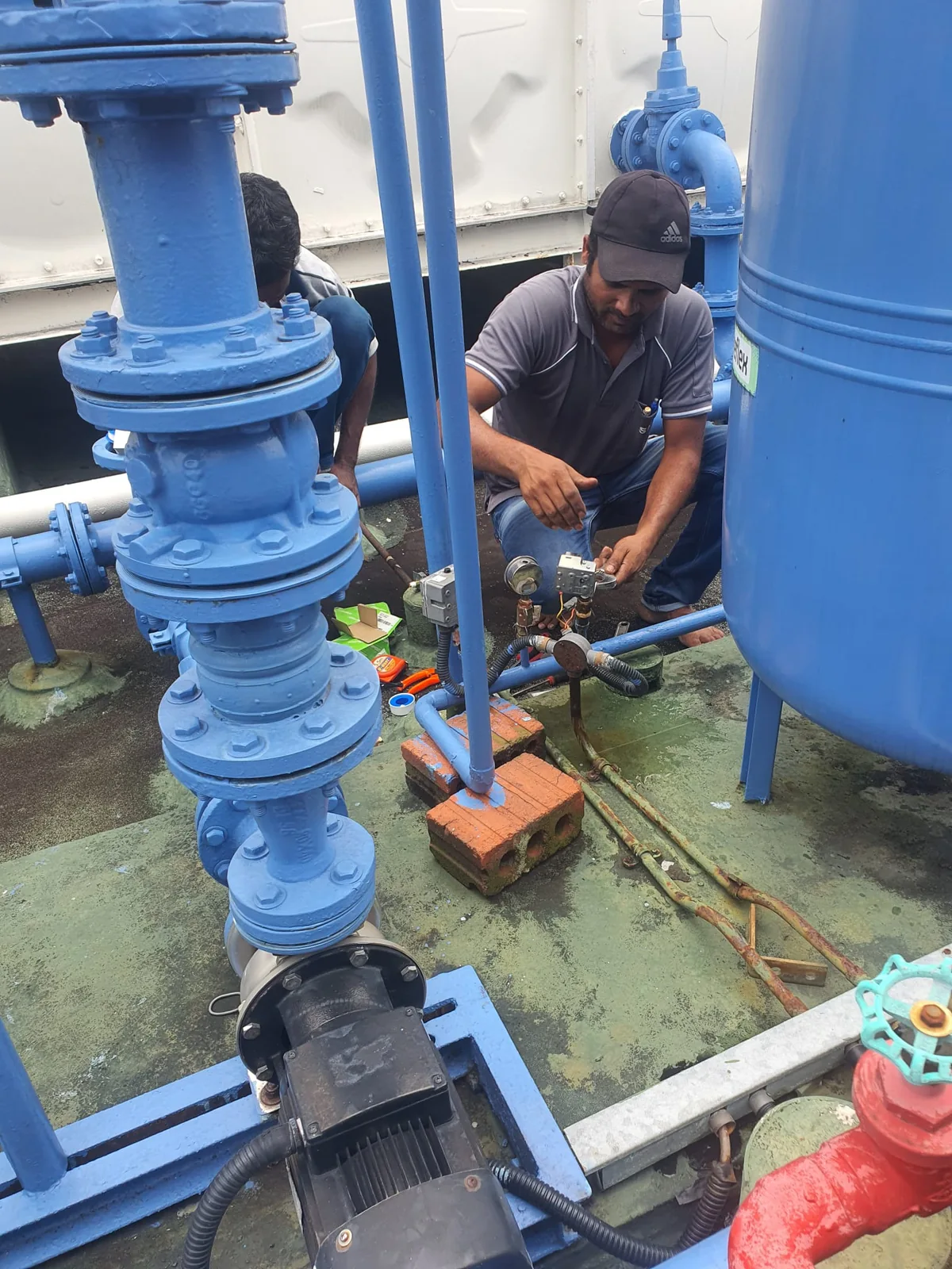 Technician servicing a pump beside blue pipework